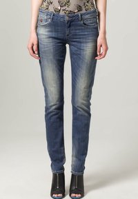 Jeans in denim blu scuro con aree sbiadite, design a gamba dritta, stile a cinque tasche e dettagli di cucitura sottili. Indossati con tacchi aperti neri.