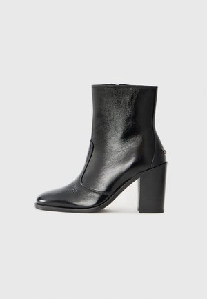 Bottine en cuir noir, avec une texture lisse, un bout pointu et un talon chunky haut. Présente une ouverture sur le côté et un design minimaliste.