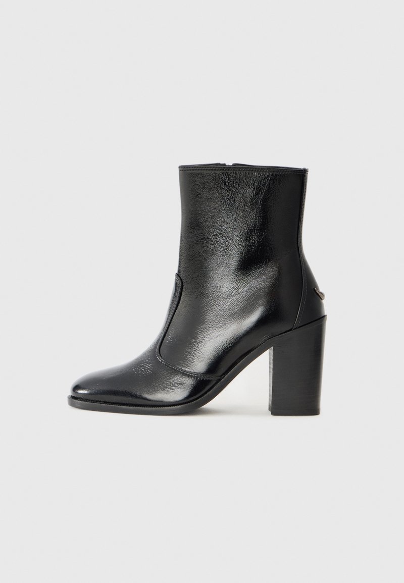 Bottine en cuir noir, avec une texture lisse, un bout pointu et un talon chunky haut. Présente une ouverture sur le côté et un design minimaliste.