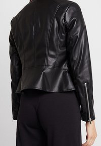 Veste en cuir noir à coupe ajustée, ourlet à basque, et accents de fermeture éclair apparente sur les côtés. Texture lisse, coutures structurées.