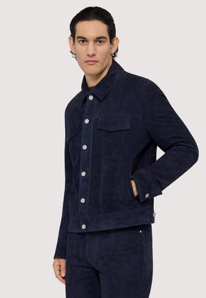 Veste en daim bleu marine avec un devant à boutons, deux poches poitrine et une coupe droite. Texture lisse avec des boutons-pression en métal.