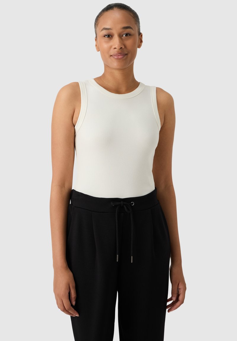 Top de tirantes blanco acanalado con escote redondo, combinado con pantalones negros con cordón. El conjunto presenta un diseño ajustado y una textura suave.