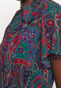 Flerfärgad skjorta med paisleymönster i rött, grönt och blått. Lätt tyg med avslappnad passform och volangärmar.