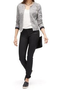 Cardigan de punto gris con cremallera plateada, camiseta blanca, pantalones negros ajustados y zapatos de lona negros. El accesorio incluye un collar de cadena plateada.