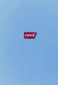 Petite étiquette logo Levi's rouge cousue sur un tissu bleu clair, probablement une partie d'un vêtement.