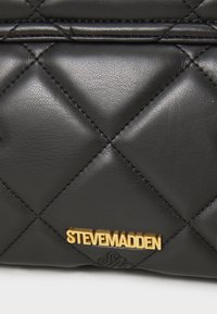 Čierna prešívaná kožená kabelka so zlatými doplnkami a logom "STEVE MADDEN". Hladký povrch s diamantovými vzormi a šitými detailmi.