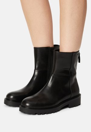 Stivaletti alla caviglia in pelle nera con texture liscia, dettaglio con cerniera laterale e suola in gomma chunky con motivo a tasselli.