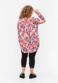 Blouse colorée à manches longues avec des motifs abstraits roses, bleus et oranges, associée à des leggings noirs coupés avec des bordures en dentelle et des chaussures noires.