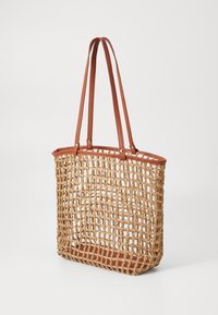 Bolsa de paja trenzada con asas de cuero marrón. Diseño abierto, forma rectangular y base sólida de cuero. Paleta de colores naturales.