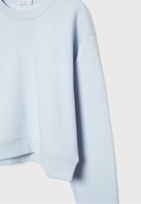 Sweat-shirt court bleu clair en coton doux. Présente un col rond et des poignets côtelés, avec une coupe décontractée et une texture lisse.