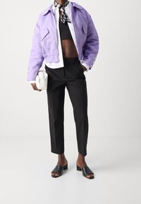 Krátká levandulová bunda, černý crop top, dobře střižené černé kalhoty a černé klouzavé sandály. Malá bílá kabelka a vzorovaný šátek jako akcent.