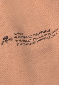 Peach-colored fabric with a smooth texture features black printed text stating "Achiote: Flowers to the People" and care instructions.