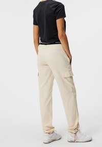 Pantalones cargo beige con bolsillos laterales, piernas con corte ajustado, cintura elástica, combinados con una camiseta negra de manga corta y zapatillas blancas.