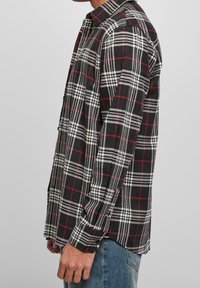 Camicia in flanella a quadri bianco e nero con dettagli rossi, colletto button-down, maniche lunghe e vestibilità rilassata, realizzata in un tessuto texture.