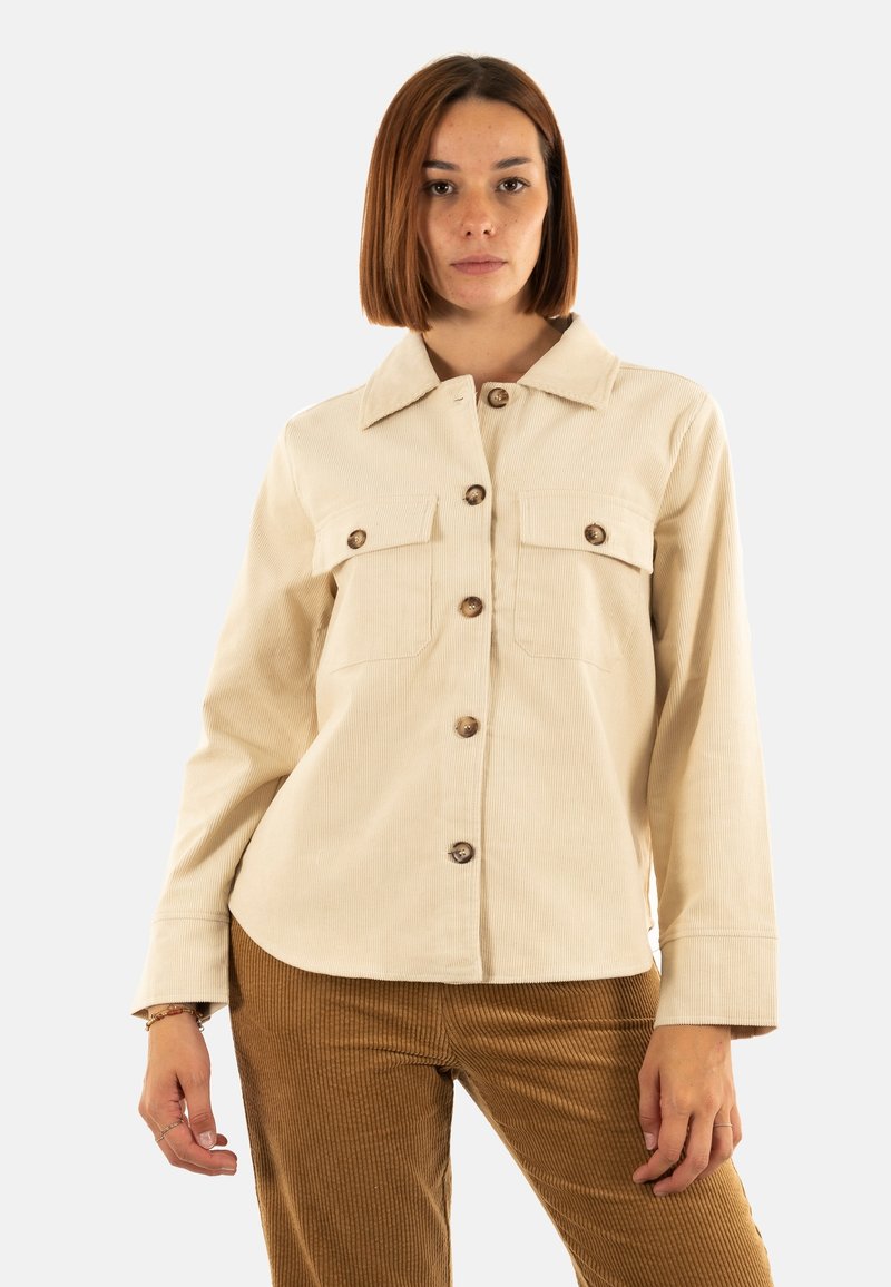 Camisa chaqueta de pana color crema con cuello, cierre de botones en la parte delantera y dos bolsillos en el pecho. Presenta botones marrón claro y mangas largas.