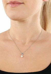 Silverhalsband med en delikat kedja som har en rund vit pärlpendel och en liten dekorativ utsmyckning ovanför pärlan.