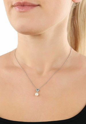 Collana d'argento con una delicata catena che presenta un pendente a forma di perla bianca tonda e un piccolo ornamento decorativo sopra la perla.