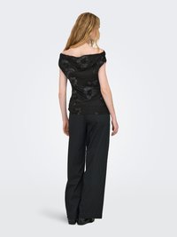 Schwarzes schulterfreies Oberteil mit Blumenstickerei, kombiniert mit lockeren schwarzen Hosen. Der Stoff wirkt glatt und leicht glänzend.