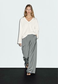 Losse witte V-hals top met lange mouwen, gecombineerd met hoge grijze wijde broek. Minimalistisch ontwerp met een zachte textuur.