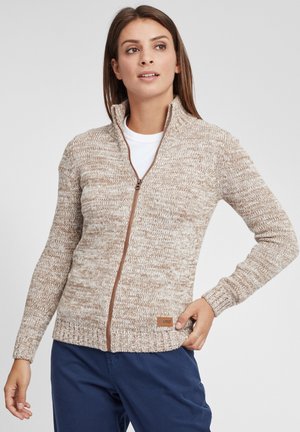 Pull en maille beige à zip, avec un motif texturé, des manches longues et des poignets côtelés. Il présente une fermeture éclair marron et une étiquette de marque dans l'ourlet.