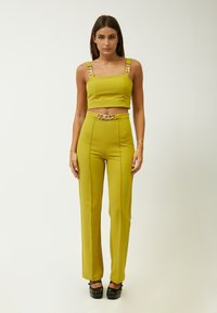 Geel tweedelig set met een cropped top met kettingaccenten op de bandjes en hoge taille broek met een kettingriem. Soepele stof, perfecte pasvorm.