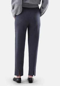 Dunkelgraue, elastische Hosen mit Seitenschlitzen am Saum, aus weichem Stoff. Kombiniert mit schwarzen Slippers.