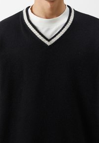 Czarny sweter z dzianiny z głębokim dekoltem w serek, z paskowanym kołnierzem w białym i szarym kolorze. Tekstura wydaje się miękka i przytulna.