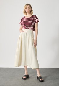 Striped burgundy and white short-sleeve shirt paired with a cream, pleated midi skirt and black platform sandals on a gray surface.