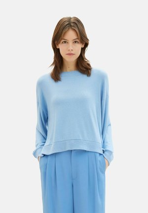 Pull en maille oversize bleu clair avec un col rond, des épaules tombantes et un ourlet côtelé. Assorti à un pantalon bleu ample.