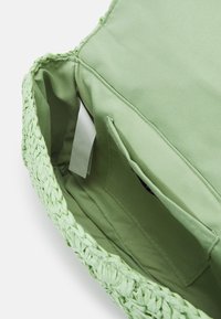 Wnętrze zielonej plecionej torby z gładką podszewką, kieszenią po jednej stronie i kontrastową fakturą w porównaniu do plecionego zewnętrza.