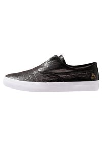 Baskets slip-on avec tige en cuir texture crocodile noir et semelle en caoutchouc blanche, présentant un petit logo triangulaire doré près du talon.