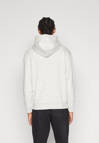Felpa grigia chiara con un ampio cappuccio foderato; polsini e orlo a coste; texture morbida; indossata con jeans scuri; vista posteriore semplice.