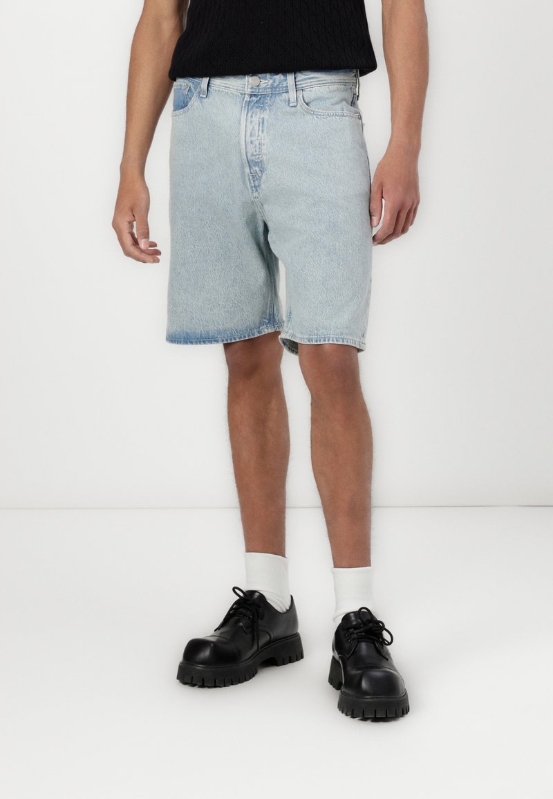 Light blue denim shorts with a relaxed fit, frayed hems, and standard five-pocket design, paired with black chunky shoes and white socks.