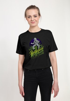 Zwarte t-shirt met een grafisch ontwerp van een figuur in gestreepte kledij. De tekst luidt "Beetlejuice" in het groen, met een paarse cirkelachtergrond.