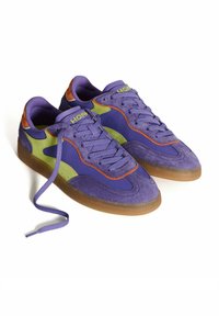 Zapatillas de ante moradas con acentos en verde y naranja, que cuentan con una suela de goma, cordones planos y un cuello acolchado para mayor comodidad.