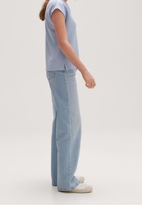 Světle modrý vroubkovaný top s krátkým rukávem v kombinaci s vysokými, širokými džínami ze světle modré denimu a bílými teniskami. Viditelná textura a střih.