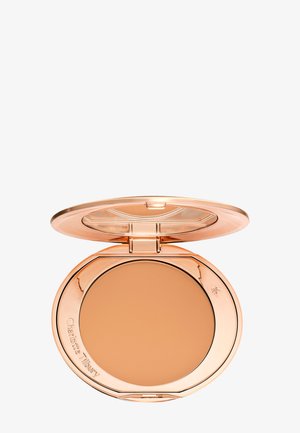 Compact de poudre pressée avec un boîtier métallique doré. L'intérieur contient une poudre beige lisse et présente le nom de la marque gravé.