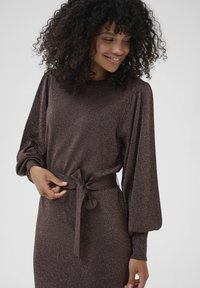 Robe tricotée brune et étincelante avec de longues manches volumineuses et une taille nouée. Présente un col rond et une texture douce.