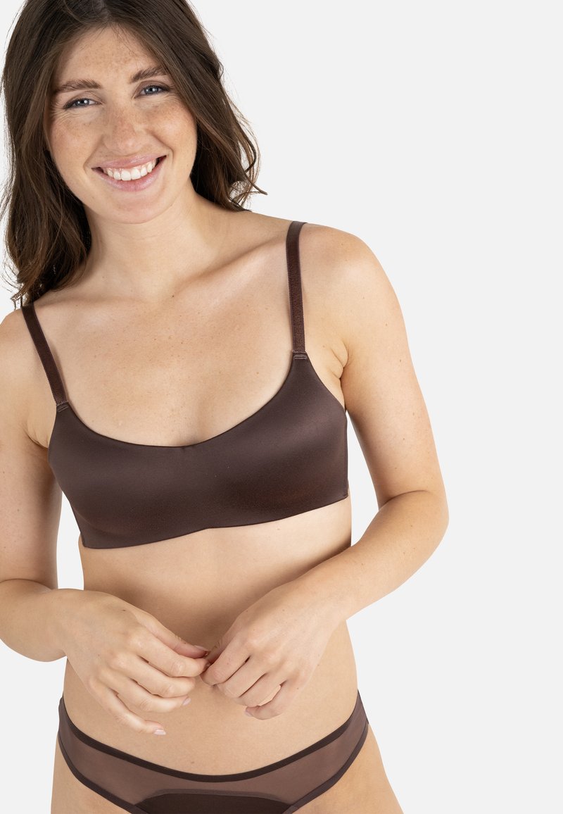 Brown seamless bra with thin straps, smooth texture, and minimal design. Paired with sheer brown underwear, featuring slight pattern contrast.