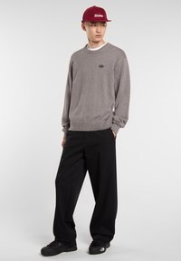 Maglione grigio a maglia con orlo a coste, abbinato a pantaloni neri a gamba larga. Cappello bordeaux con logo "Dickies". Calzature nere con suola testurizzata.