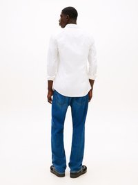 Hvit langermet skjorte med klassisk krage, kombinert med løse blå denimjeans og svarte sandaler. Glatt stoff, avslappet passform og rett ben-design.