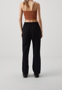 Černé kalhoty s elastickým pasem v kombinaci s krátkým topem vzorovaným červenými vlnitými pruhy na světlem pozadí, pohled zezadu.