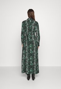 Långärmad grön och svart mönstrad klänning med knytmidja, flödande design och ankellång nederdel, kombinerad med svarta klackstövlar.