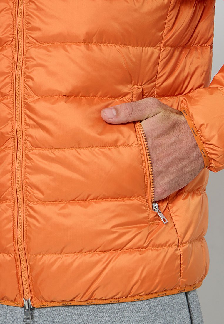 Orangen gepolsterte Jacke mit Reißverschluss, die über eine Taschen an der Seite und elastische Bündchen verfügt. Glattes, glänzendes Material mit Nähdetails.
