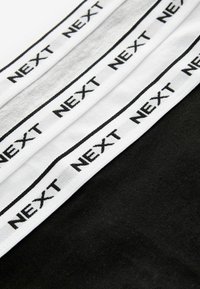 Fasce elastiche nere e bianche con la scritta "NEXT" stampata in nero, disposte in piano, mostrando una superficie liscia e un design pulito.