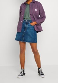 Chaqueta de algodón morada, camiseta de cuello en V verde, falda de mezclilla en línea A y zapatillas negras de caña alta. Textura suave, ajuste casual y detalles de botones.