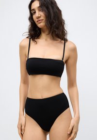 Μαύρο μπικίνι σετ με τοπ μπαντό που έχει λεπτές τιράντες και σλιπ ψηλής μέσης. Κατασκευασμένο από λείο, ελαστικό ύφασμα με μινιμαλιστικό σχέδιο.