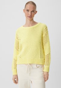 Gelb gestrickter Pullover mit Lochmuster, weitem Ausschnitt und gerippten Bündchen. Leichte Textur, cropped Design, kombiniert mit hellen Hosen.