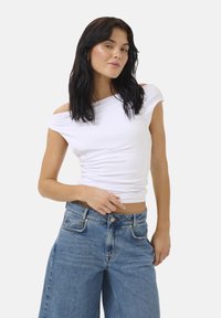Top bianco con spalle scoperte e design arricciato ai lati; abbinato a jeans a gamba larga di un blu chiaro a vita alta con chiusura a bottone.
