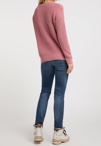 Růžový pletený svetr s volným střihem, se žebrovaným lemem a manžetami. V kombinaci s tmavě modrými skinny džíny a bílými kotníkovými botami s šedými akcenty.